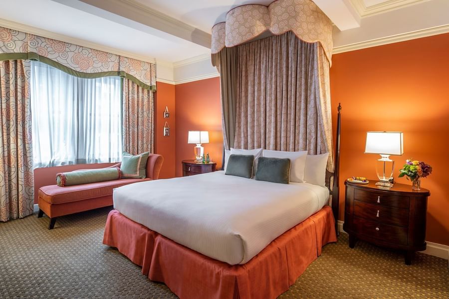 Elegantly furnished hotel room with a king-sized bed, chaise lounge, and wooden nightstands at Warwick New York