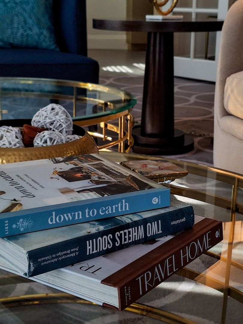 Stack of books on a glass table by a gold bowl under a soft light in Presidential Suite at Warwick Melrose Dallas