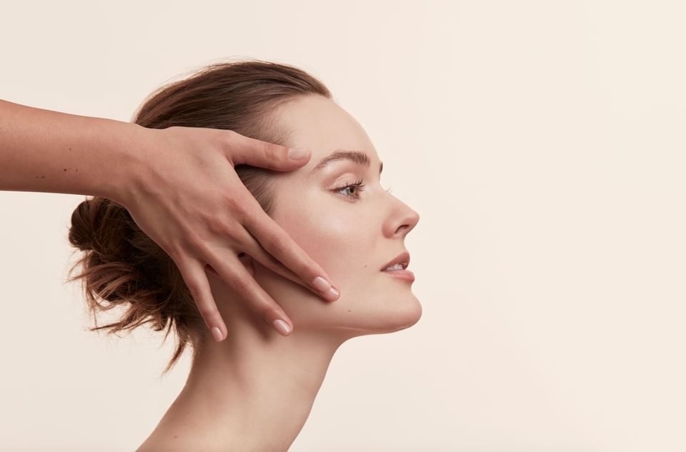 Profile view of woman receiving relaxing facial massage treatment with hands gently framing face at Hotel X Toronto