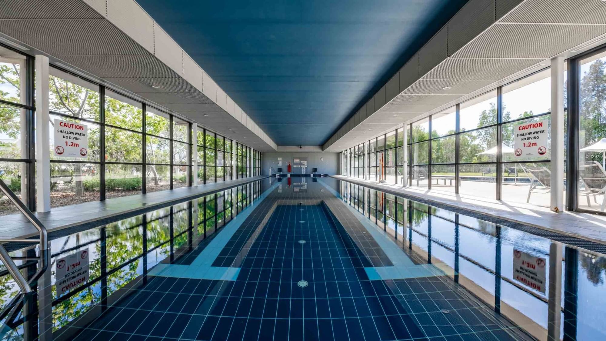 Indoor lap pool with reflective water, and large windows at Mercure Kooindah Waters