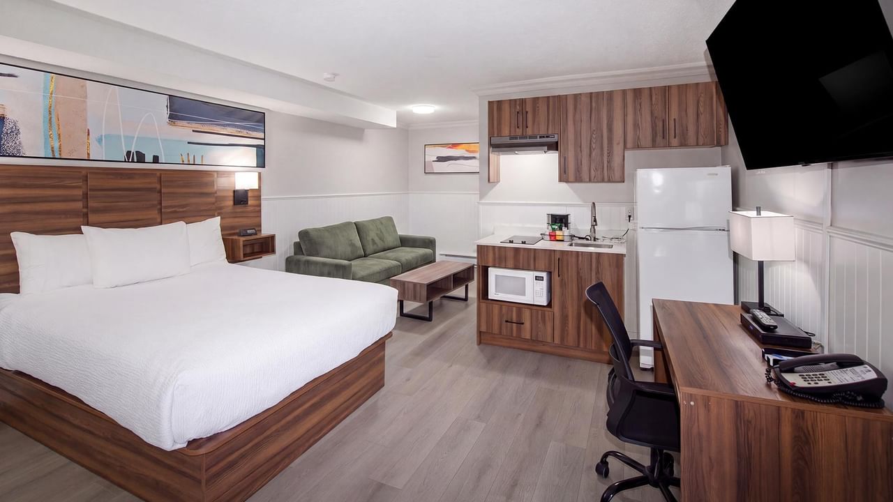 Modern hotel room with a queen bed, seating area, kitchenette and work desk.