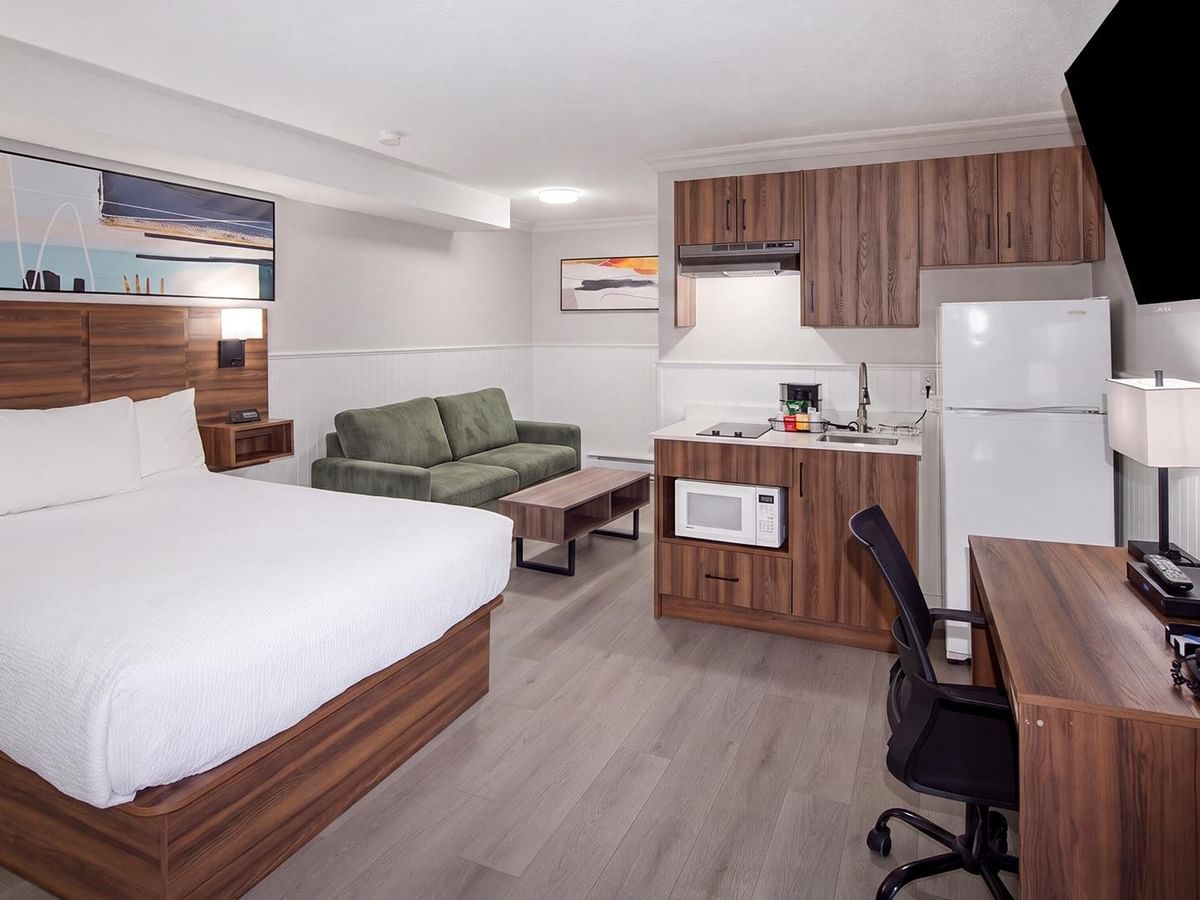 guest room with a queen bed, sofa, kitchenette, work desk and wall-mounted flat-screen TV at Coast Dawson Creek Hotel