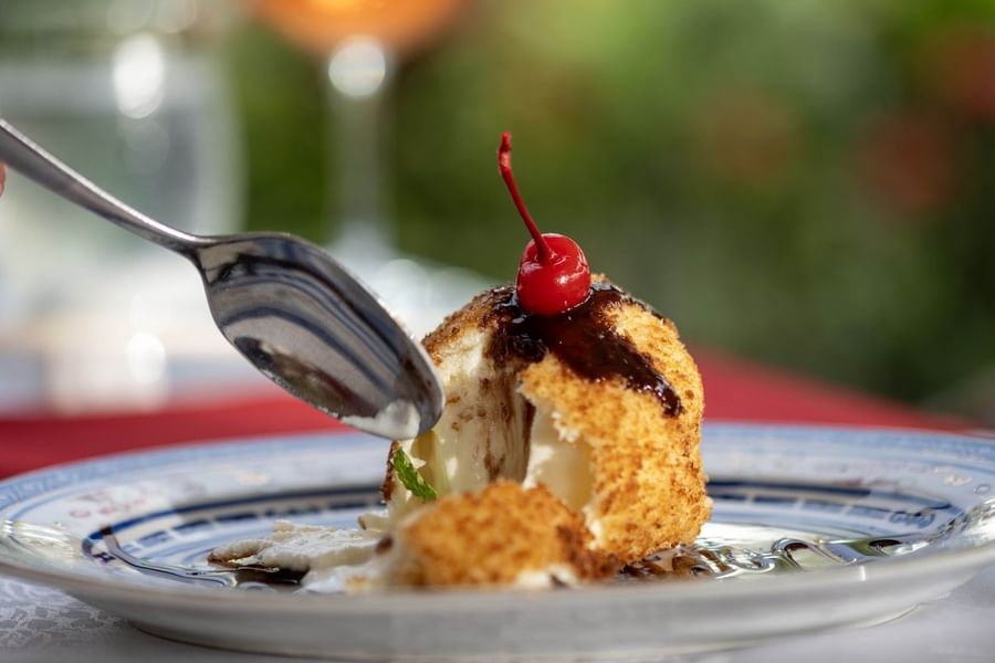 Fried dessert with a cherry on top by a silver spoon on a plate in Bamboo Terrace at The Naviti Resort - Fiji