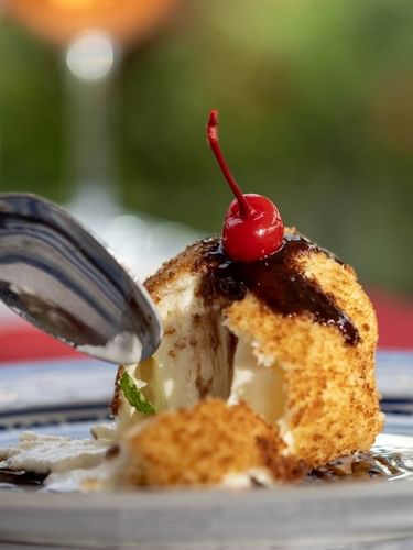 Fried dessert with a cherry on top by a silver spoon on a plate in Bamboo Terrace at The Naviti Resort - Fiji