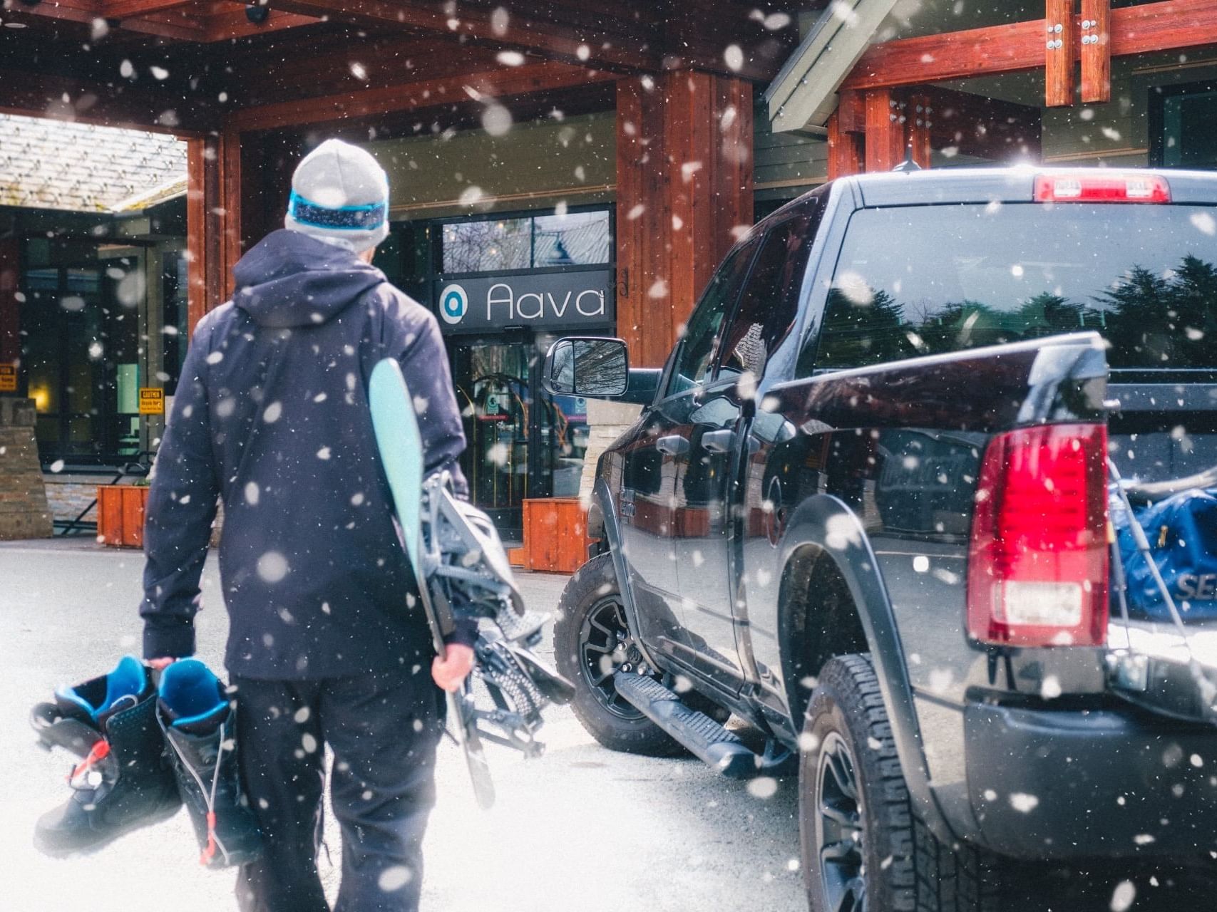 Man with snowboard and boots walking to Aava Hotel in the Snow.