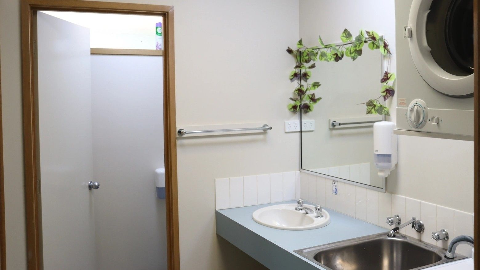 Bathroom with open shower stall, sink, mirror, and washing machine visible.