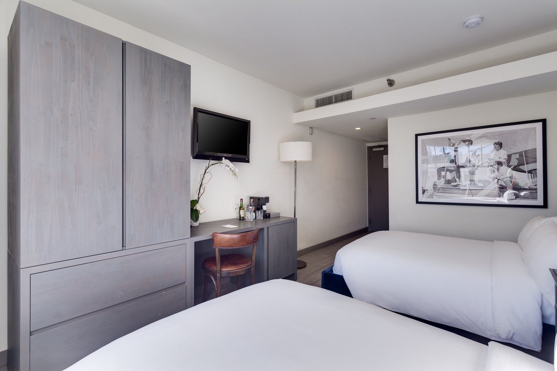 A clean and modern hotel room with two beds, a desk, and a large closet.