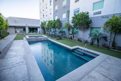 Outdoor swimming pool by green trees under facade of the Hotel Mirra, stopover hotel San Luis Rio Colorado on road trip