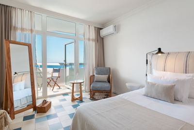 Bedroom with balcony, wicker chair, white bed, blue and white checkered floor, and ocean view.