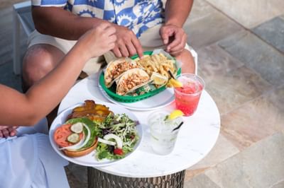 Close-up of a couple enjoying lunch with tacos, fries, and cocktails at a small table at the Maui Coast Hotel