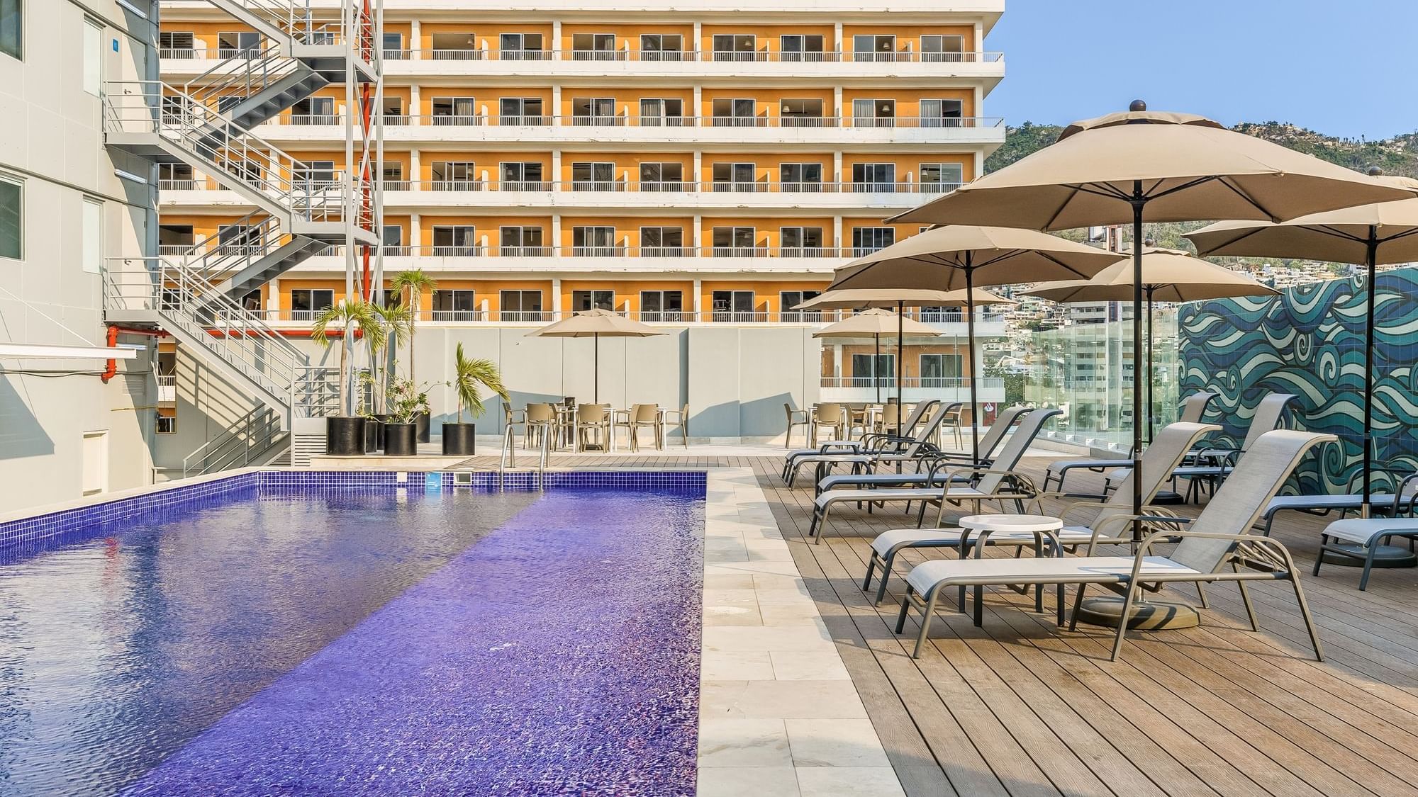 Outdoor pool area with sun loungers & patio umbrellas at One Acapulco Costera