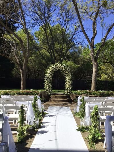 Outdoor wedding ceremony setup with a white aisle runner,chairs, and a floral archway at Lake Natoma Inn