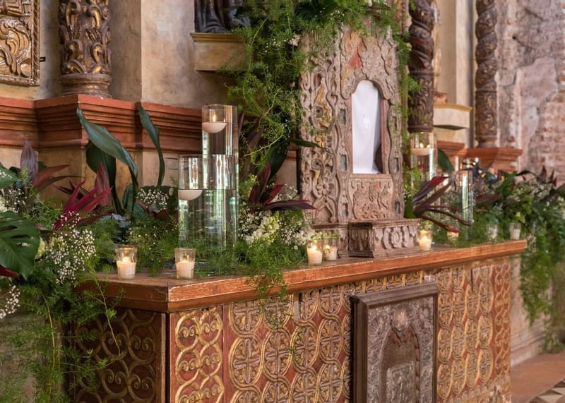 Altar adornado con follaje verde, acentos rojos y pequeñas velas que crean un ambiente sereno en Casa Santo Domingo