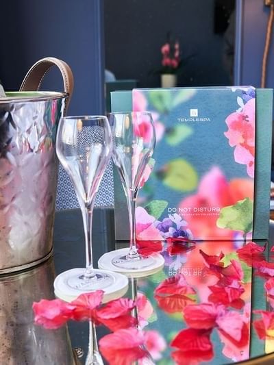 Champagne bucket by two glasses on a mirrored table, surrounded by red petals at The Capital Hotel, Apartments and Townhouse
