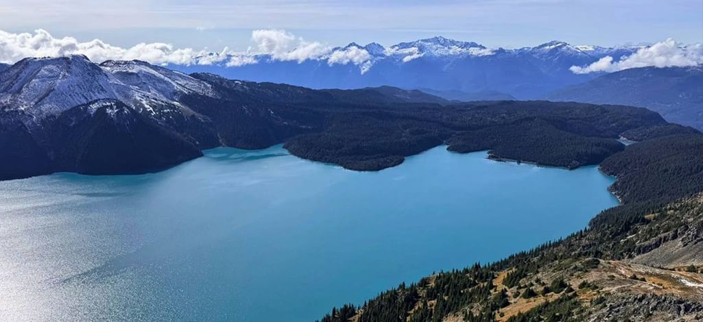 Sweeping view of turquoise Garibaldi Lake surrounded by forested mountains and snow-capped peaks.