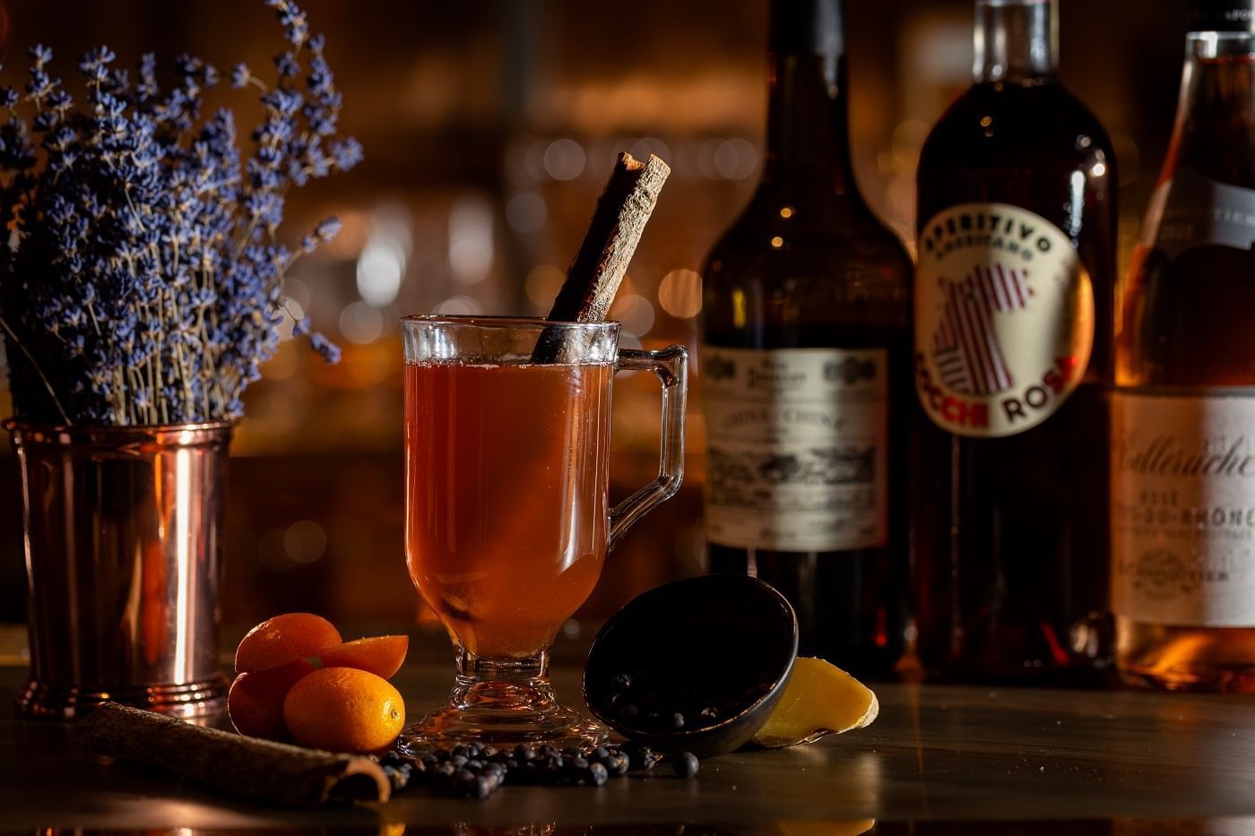 A warm, inviting cocktail with a cinnamon stick garnish, surrounded by rum bottles in Joshua\'s Tavern at The Londoner Hotel