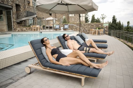 A couple lying in lounge chairs by the infinity pool at Stein Eriksen Residences