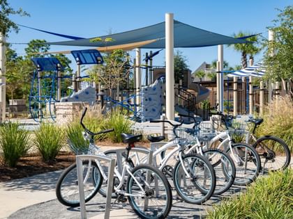 Complimentary bikes parked near a shaded playground with climbing structures at Camp Creek Inn in Inlet Beach.