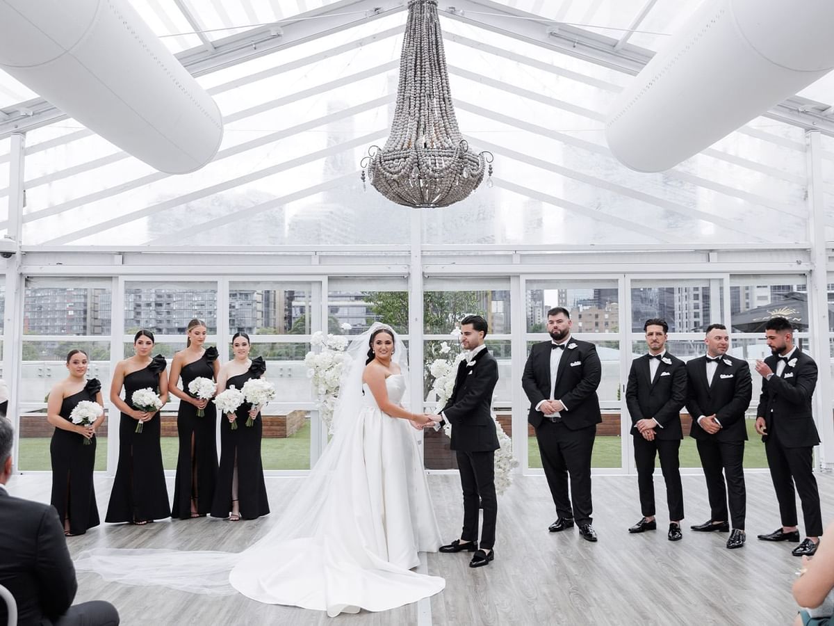 Clarissa and Kristian posing with their group in a wedding hall with a glass ceiling at Crown Towers Perth