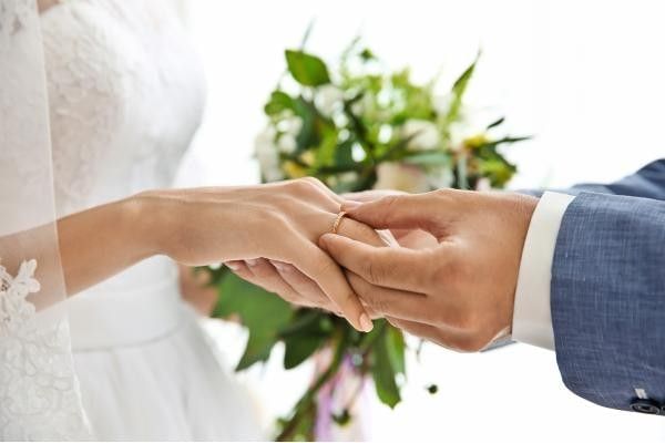Groom placing wedding ring on bride featuring our article on "do you wear your engagement ring on your wedding day"