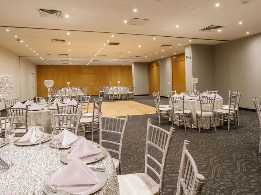Milan banquet hall featuring round tables with silver chairs and a small wooden dance floor at Real Inn Torreon