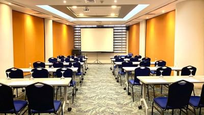 Centenario Meeting Room with chairs and desks arranged for a meeting, featuring a projector screen at Dann Carlton Cali