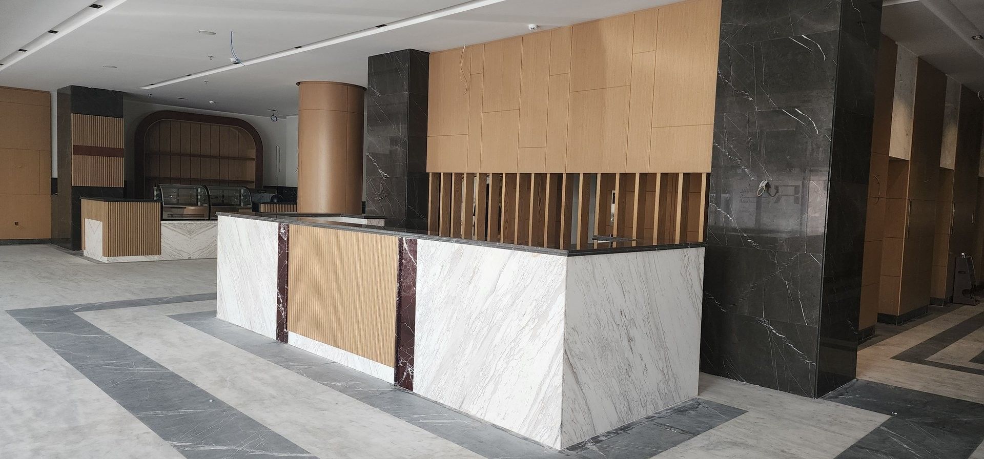 White marble reception desk with wood accents by dark stone walls under a high ceiling at Warwick Jeddah Hotel & Spa