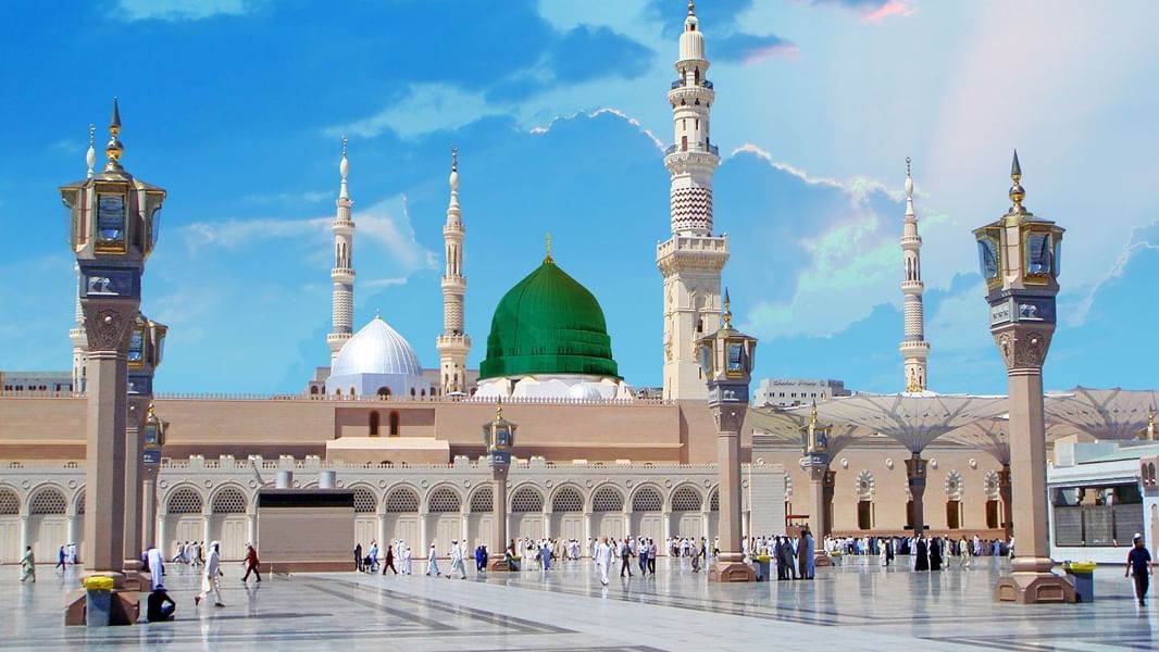 The iconic Green Dome and white minarets of Al-Masjid an-Nabawi under a bright blue sky at Saja Warwick Madinah