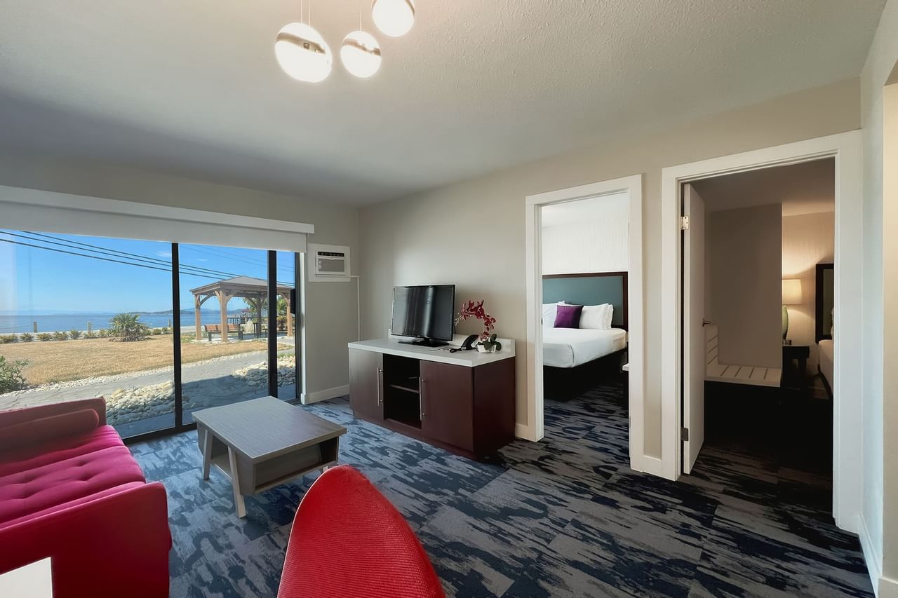 Living area of guest room with tv, coffee table, red couch, patio doors, view of sea