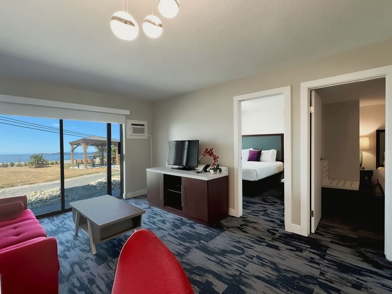 Living area of guest room with tv, coffee table, red couch, patio doors, view of sea