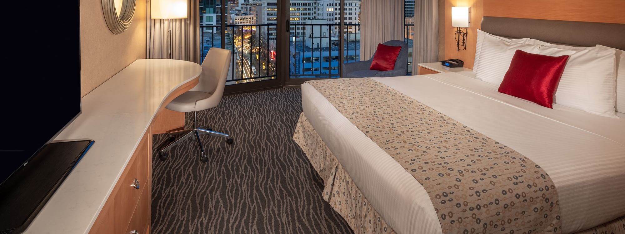 Premier room at Warwick Seattle with a large bed, balcony, chair, desk, and TV overlooking city lights.