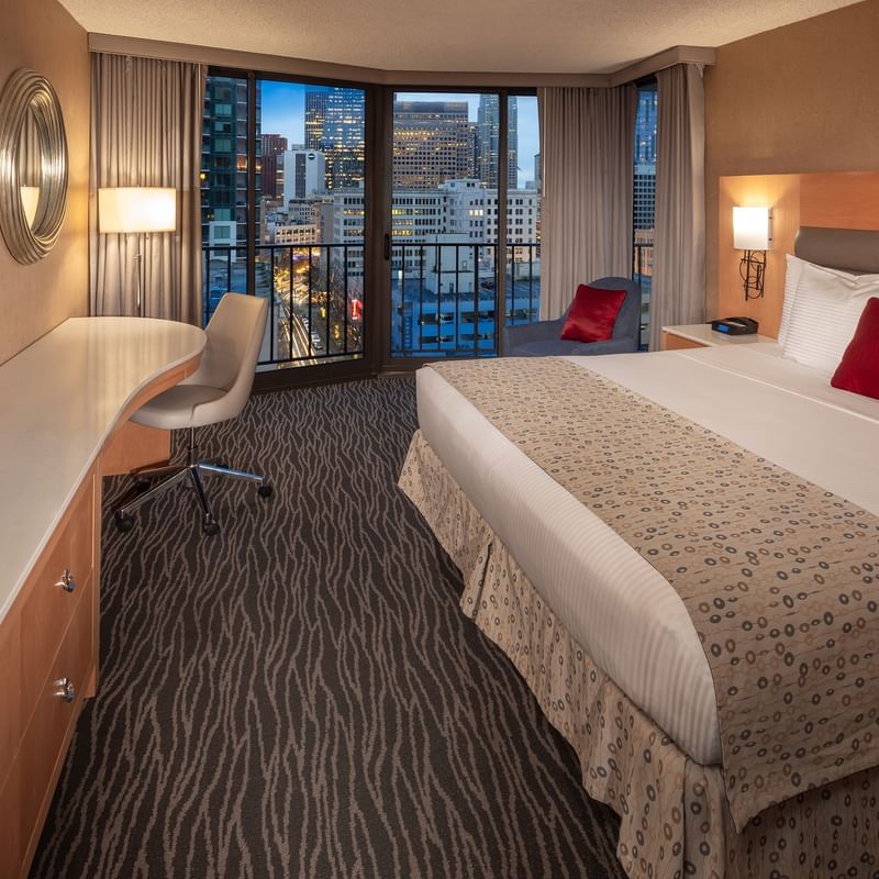 Premier room at Warwick Seattle with a large bed, balcony, chair, desk, and TV overlooking city lights.