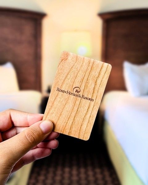 A hand holding a room key in a guest room at Rosen Inn, a family-friendly hotel near Walt Disney World Resort in Orlando.