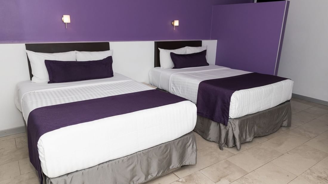Two king beds, comfy pillows & wall lamps in Junior Suite Double at Gamma Hotels