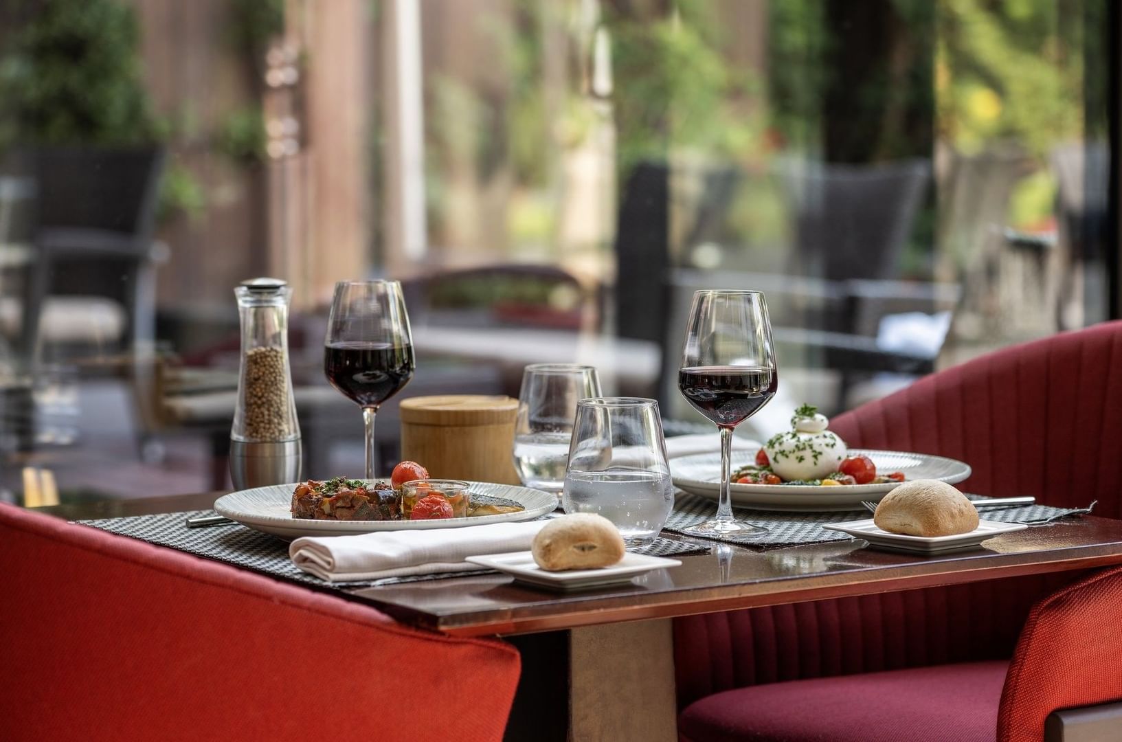 Table dressée avec plats gastronomiques, verres de vin rouge et fauteuils rouges au Warwick Reine Astrid-Lyon