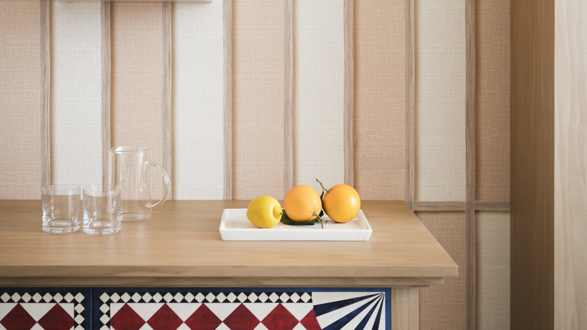 Un tavolo con una brocca, due bicchieri e un vassoio con limoni e arance.