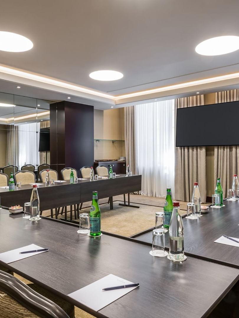 U-shaped table set up facing a hanging TV under recessed ceiling lighting in a meeting room at Warwick Grand Place Brussels