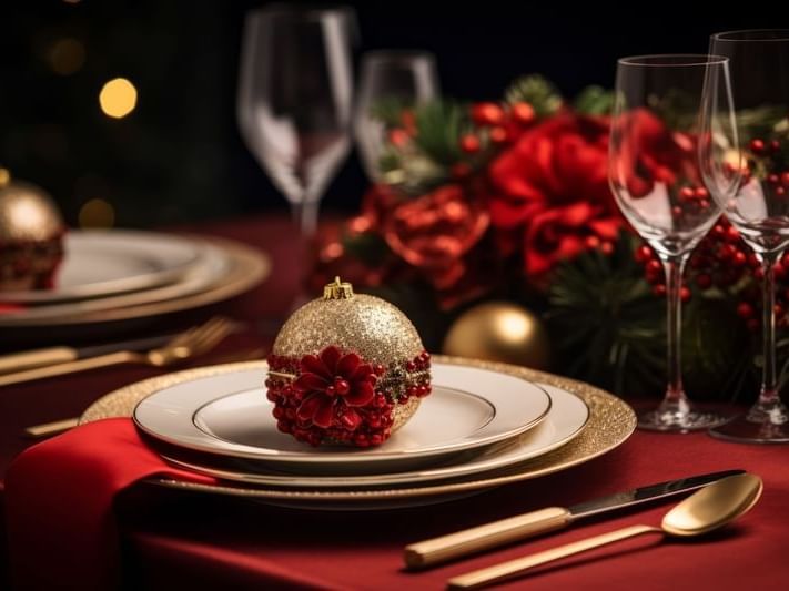 A festive table setting with red tablecloth, gold and red ornaments, and wine glasses.