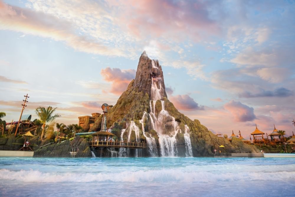 A large volcano with waterfalls cascading into a blue pool below. 