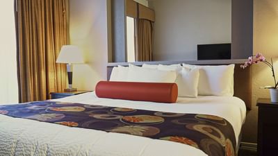 Hotel room with white bedding, red bolster pillow, decorative runner, and wall-mounted TV at London Bridge Resort