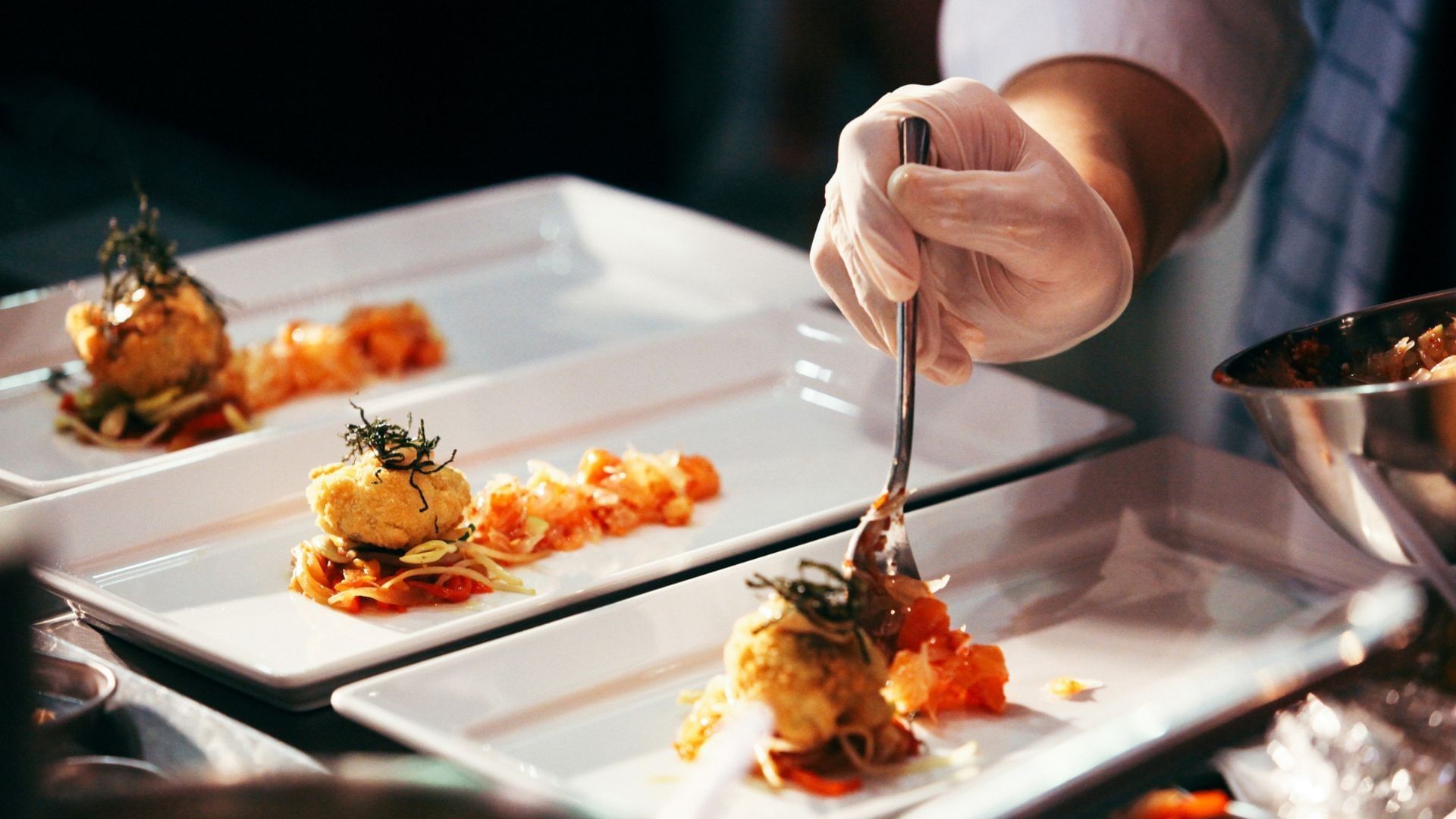 Chef garnishing plates of food with a utensil in the restaurant at A'ila Resorts