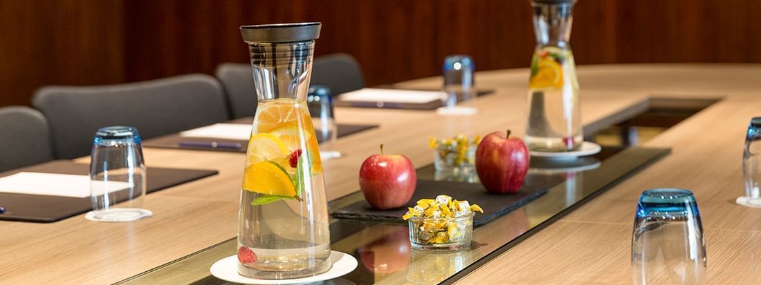 Fruit-infused water by red apples on a glass runner under warm lighting in Gobelin at Warwick Geneva