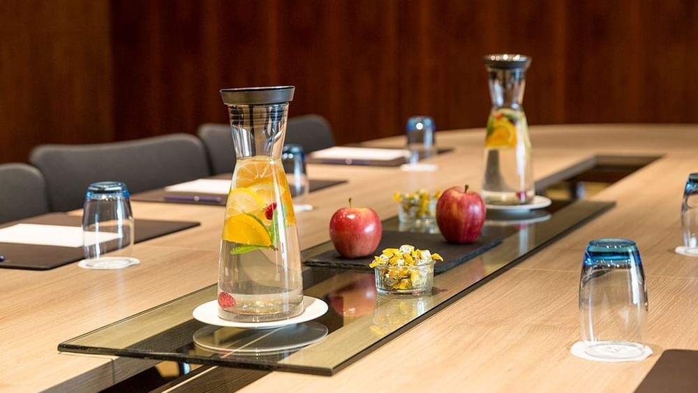 Fruit-infused water by red apples on a glass runner under warm lighting in Gobelin at Warwick Geneva