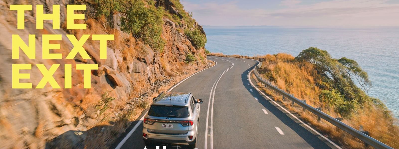 Car driving on scenic road with ocean view and Take the next exit text.