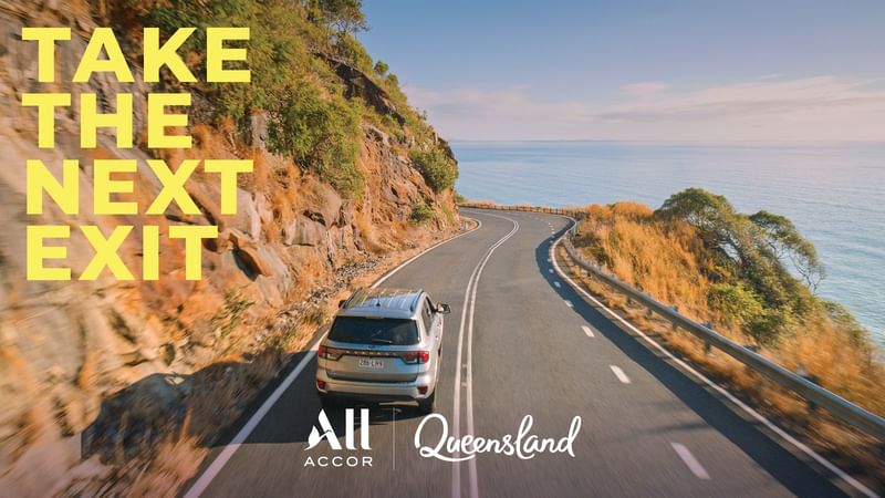 Car driving on scenic road with ocean view and Take the next exit text.