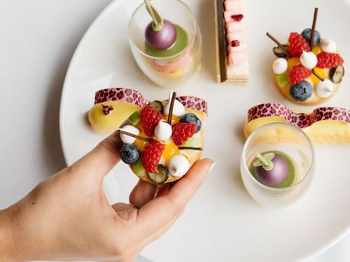 Hand holding a fruit-topped tart above a plate with assorted pastries in Restaurant Cuvée at Sofitel Brisbane Central