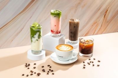 Assortment of iced matcha lattes, coffee drinks, and hot cappuccino on a table in Tuxedo Cafe at Carlton Hotel Singapore