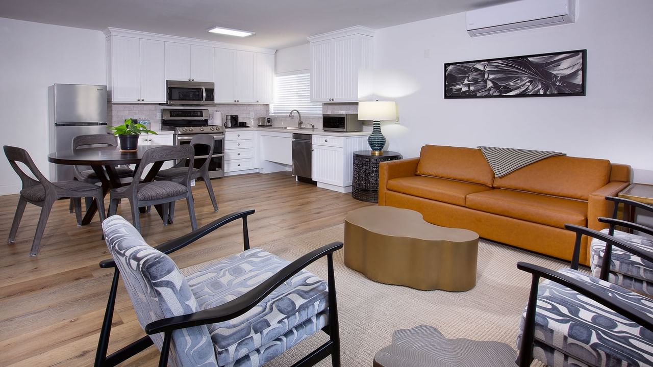 Modern living room with orange couch, dining area, and kitchen with appliances, hardwood floors, and contemporary furniture.