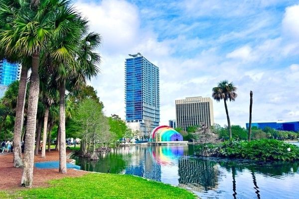 Lake Eola in Downtown Orlando with palm trees, the rainbow painted amphitheater, and tall buildings on the horizon.