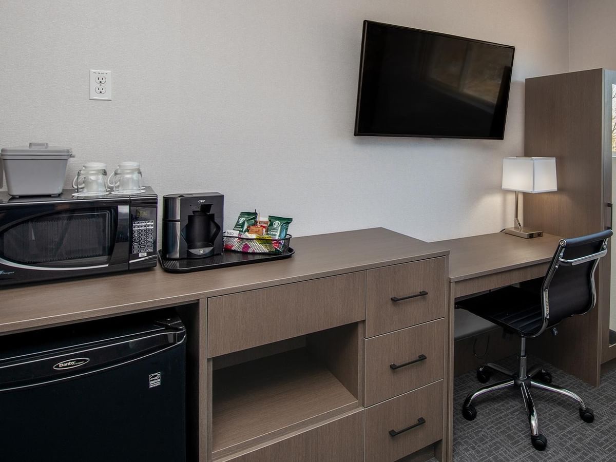Desk with microwave, fridge, coffee maker, and TV on the wall.